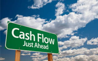 Photo of blow sky with white clouds in background. Green sign post with writing writing in foreground reads, "Cash Flow Just Ahead"