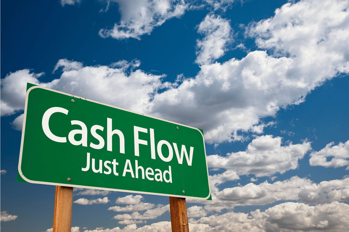 Photo of blow sky with white clouds in background. Green sign post with writing writing in foreground reads, "Cash Flow Just Ahead"